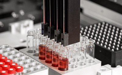 Reaction optimization A close-up view of a laboratory automation system with multiple pipette tips positioned above several glass vials containing red liquid.