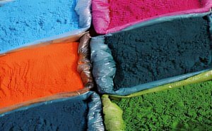 A close-up view of various colored powders arranged in bags, featuring vibrant shades of blue, pink, orange, green, and dark blue. 