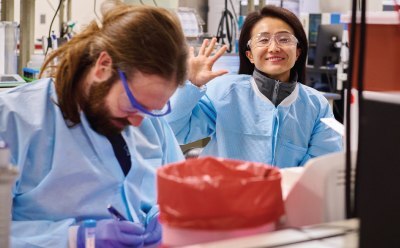 Two individuals in protective clothing collaborating in a lab setting