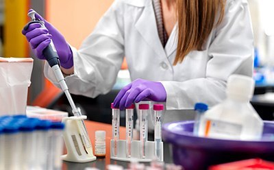 Women in lab coat with peptide, safety gloves, and safety goggles, working in a lab.