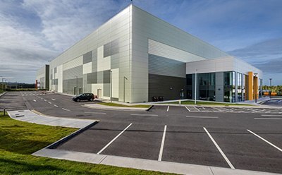 Building Exterior in Blarney, Ireland Exterior view of manufacturing facility in Blarney, Ireland, featuring a modern design with large windows and a landscaped parking area, set against a clear blue sky