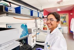 Scientist in a lab setting wearing safety glasses standing in front of a large piece of equipment Scientist in a lab setting wearing safety glasses standing in front of a large piece of equipment