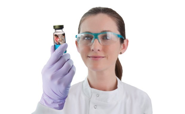A female scientist wearing protective goggles holds up a sterile drug product
