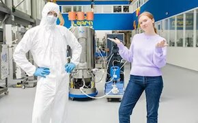 Closed Processing for Biomanufacturing Two scientists, standing in a lab, a male in bunny suit, a female wearing casual clothes