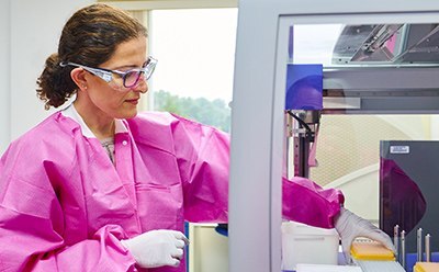 BioReliance® Blazar® Platform Female lab technician with lab protection cloth doing some testing activities with the help of a machine.