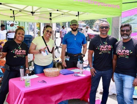 A group of employees stand together at a community event. They are standing under a company tent and smiling at the camera. A group of employees stand together at a community event. They are standing under a company tent and smiling at the camera.