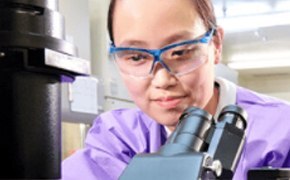 Female lab technician with Asian assemblance in lab protection cloth and working with a microscope. Female lab technician with Asian assemblance in lab protection cloth and working with a microscope.