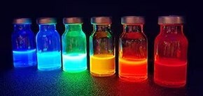 ペロブスカイト量子ドットが入った 5 つの小さなガラス瓶を UV 光で照らすと、青、緑、黄、オレンジから赤までのさまざまな色が表示され、さまざまな発光波長が示されます。